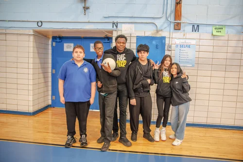 Five students posing together in school gymnasium holding volleyball