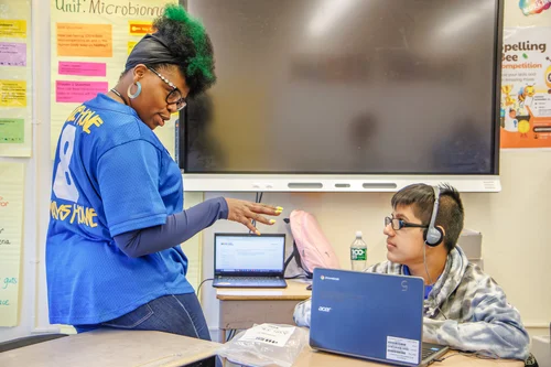 Teacher helping student working on laptop in classroom