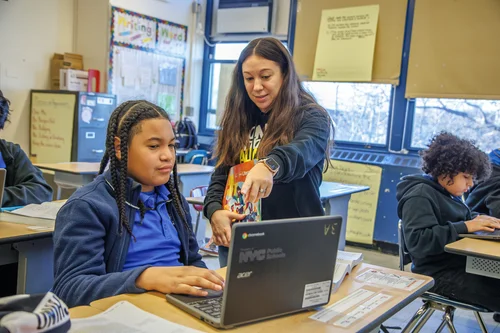 Teacher helping student with work on a laptop in classroom