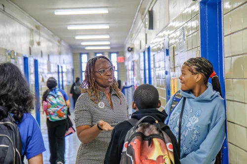 Teacher greeting a student in a busy school hallway