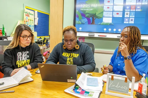 Three teachers collaborating around a laptop in a classroom