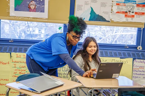 Teacher helping a student work on a laptop in class