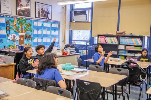 Students raising hands and engaging with teacher in classroom