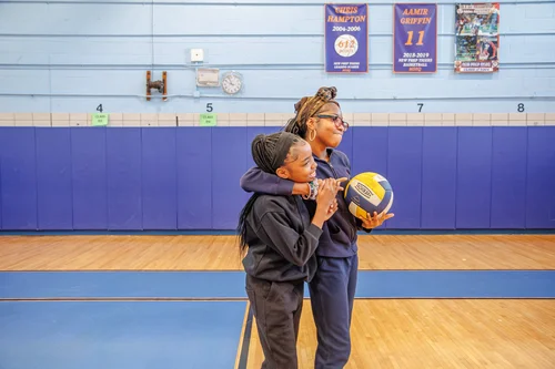 Coach and student share a moment holding volleyball in gym