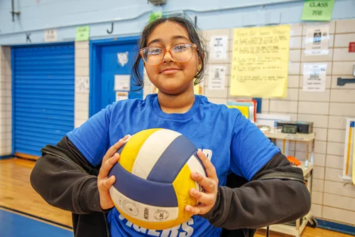 Student in blue jersey holding a volleyball in school gym