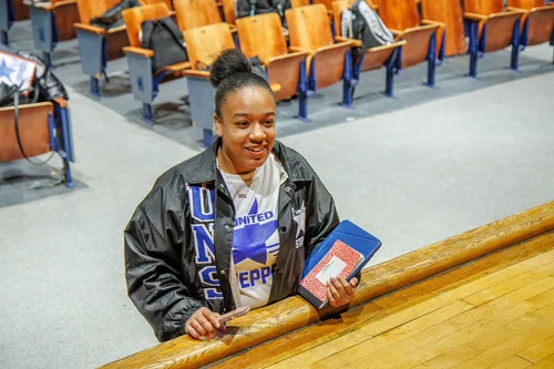 Student smiling in auditorium seating holding a notebook