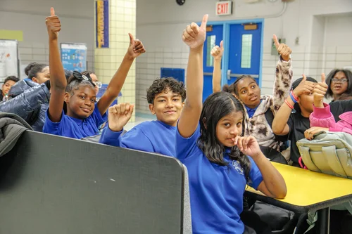 Students in blue shirts giving thumbs up in school cafeteria