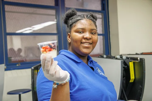 Student in blue uniform holding a cup of fruit with gloved hand