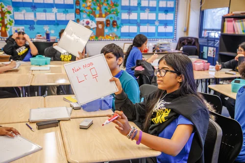 Student holds whiteboard showing Korean writing during class activity