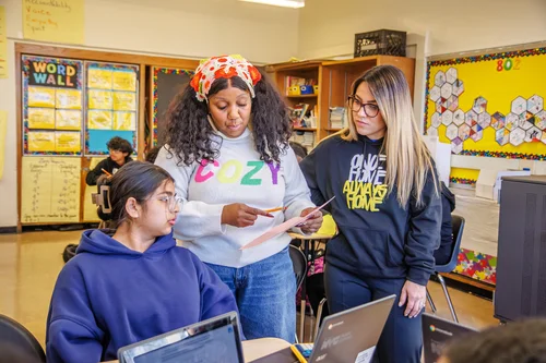 Teacher and aide helping a student with laptop work in classroom