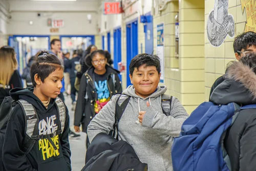 Students walking through school hallway with backpacks smiling