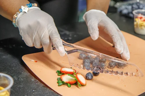 Student in gloves slicing fresh strawberries and blueberries on cutting board