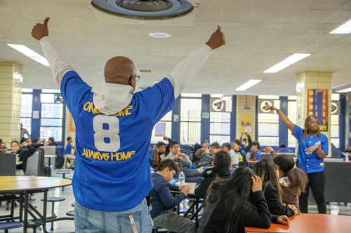 Staff member energizing students in school cafeteria wearing team jersey