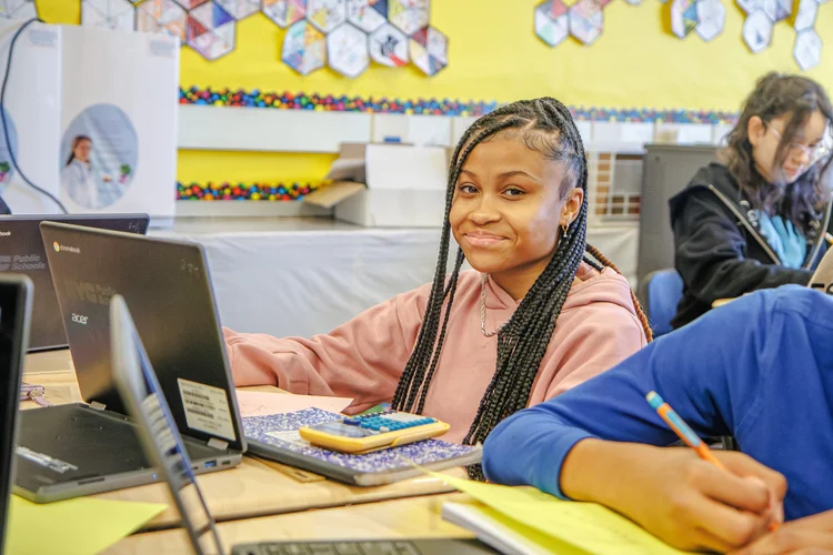 Student smiling at desk with laptop and calculator in classroom