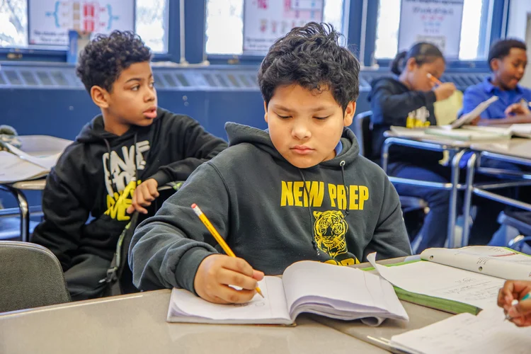 Middle school student writing in notebook during classroom lesson