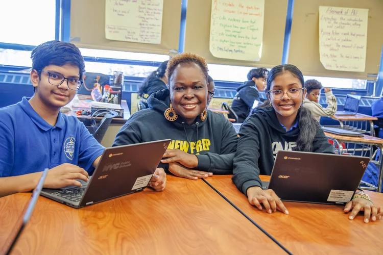 Teacher and two students smiling with Chromebooks in classroom