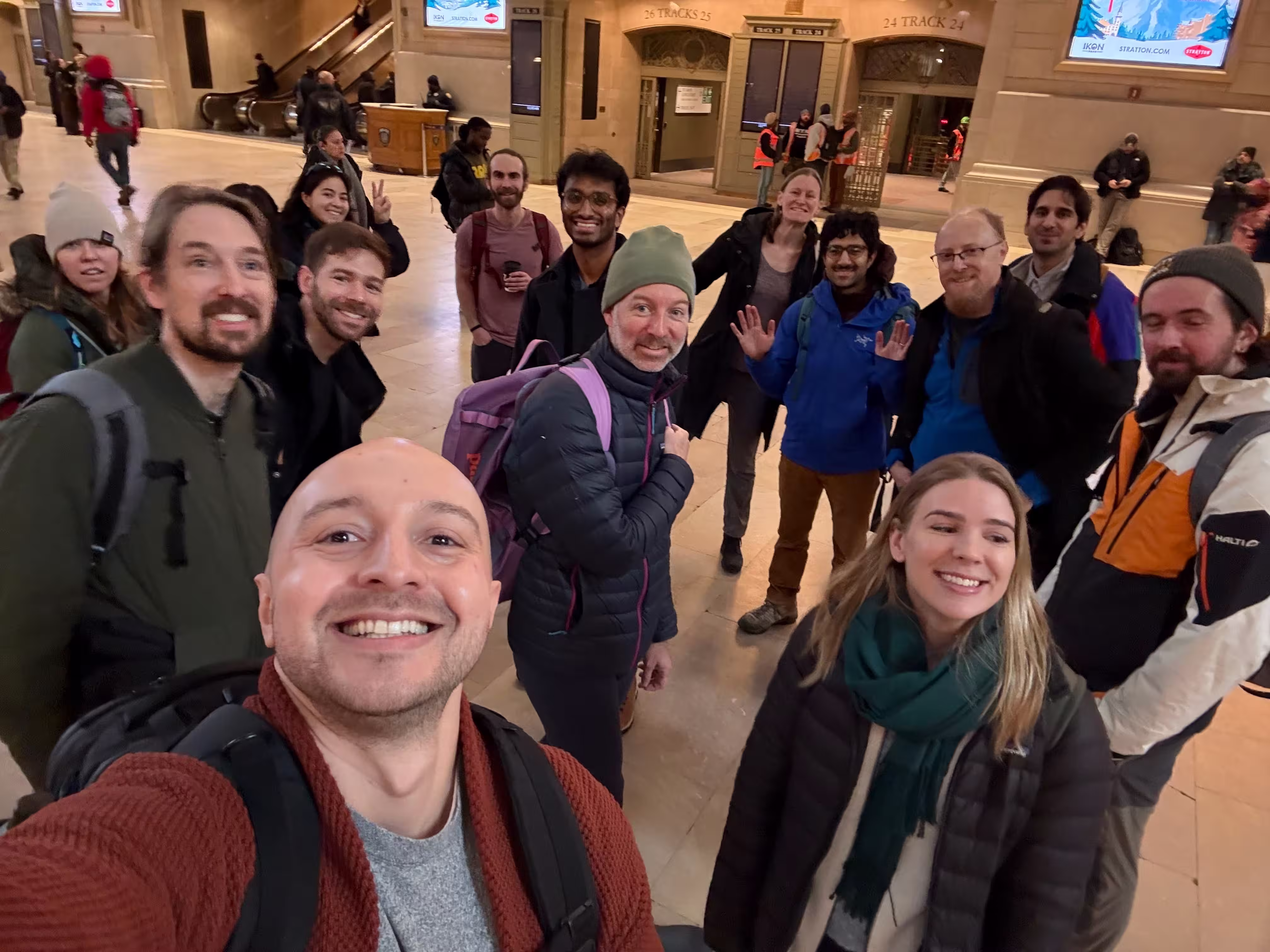 Group of people smiling and posing for a selfie in a spacious indoor train station.