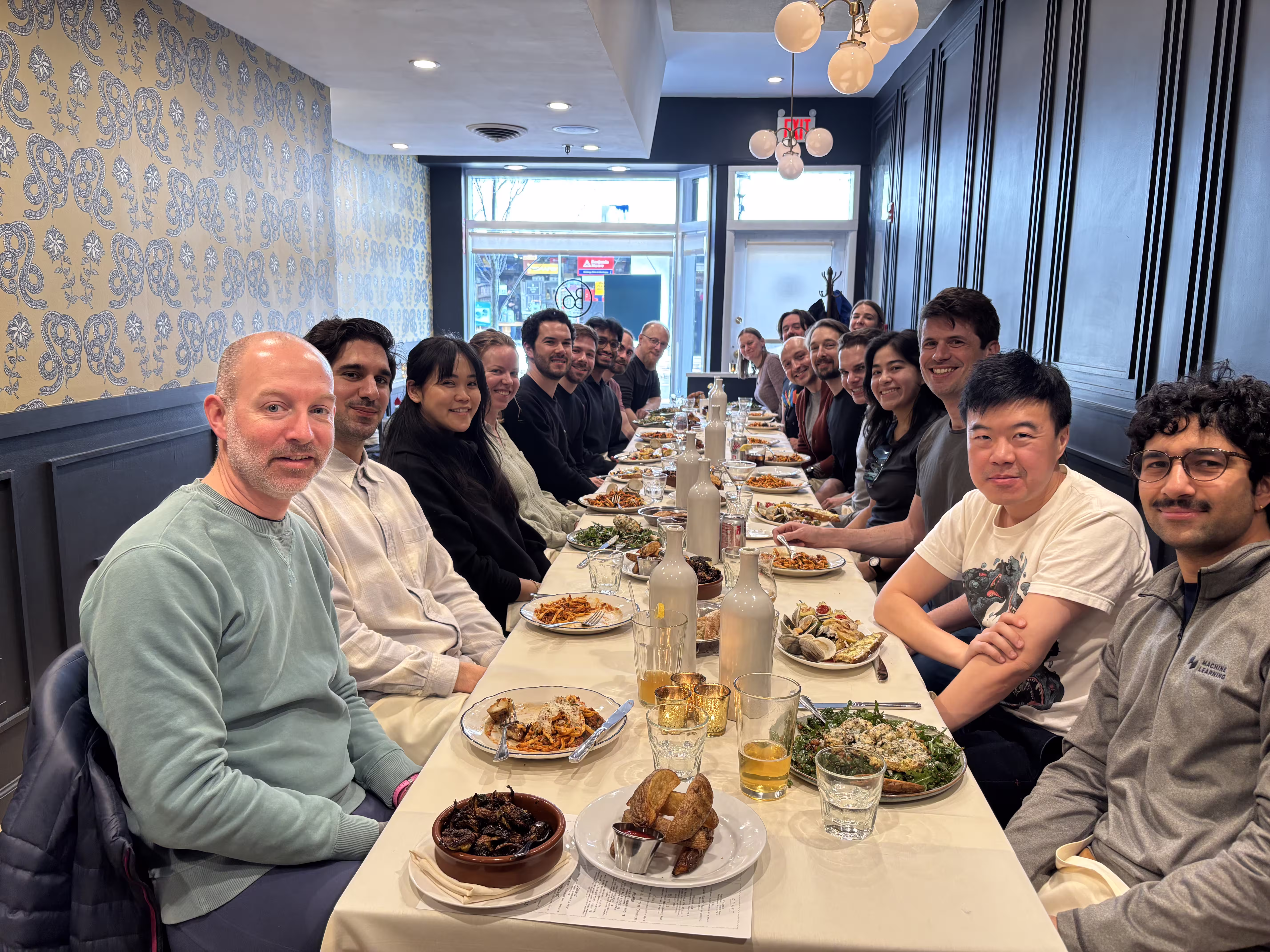 Group of people sitting at a long table with plates of food in a cozy restaurant.