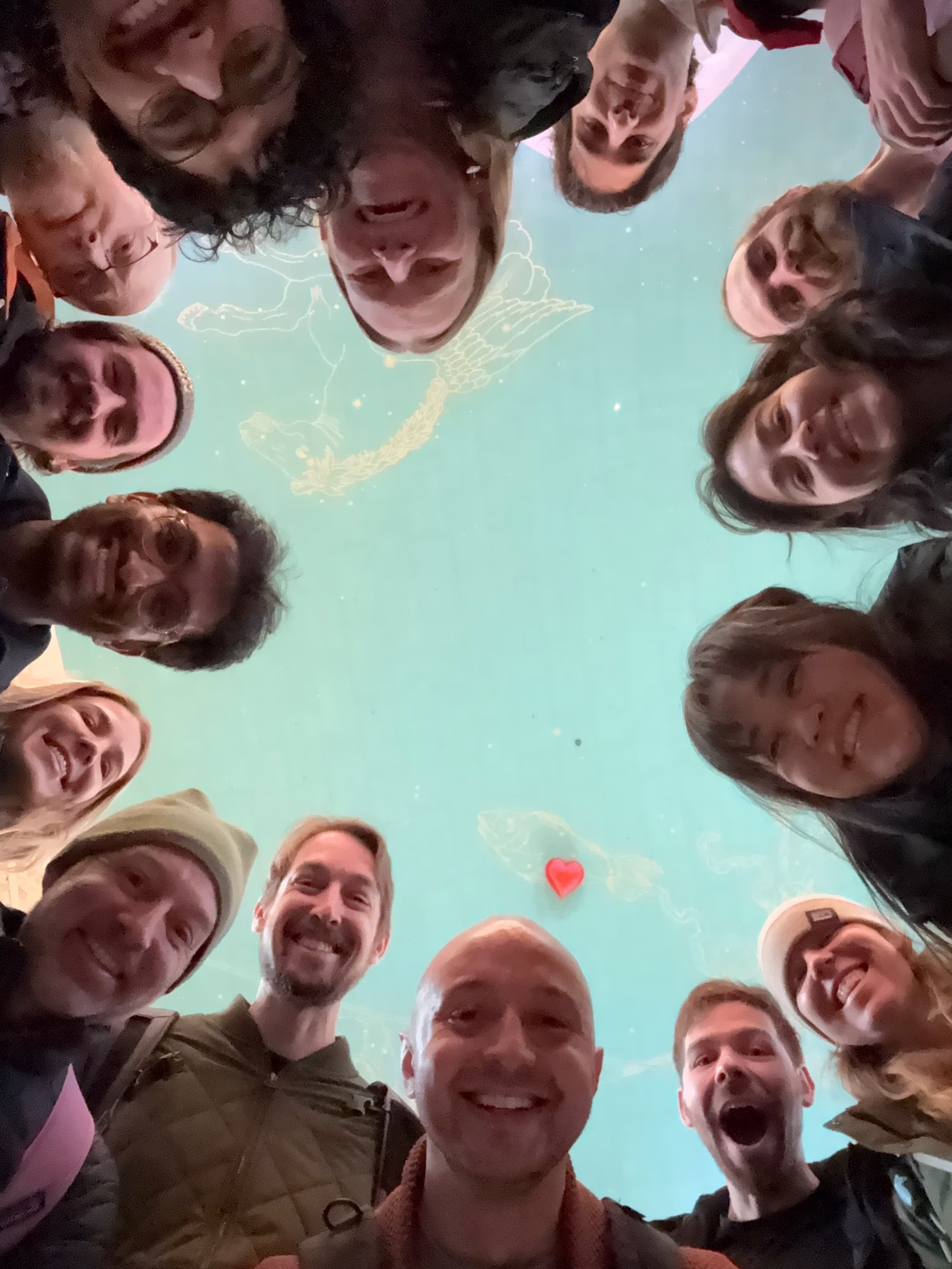 Group of people smiling, forming a circle looking down at the camera against a starry ceiling.