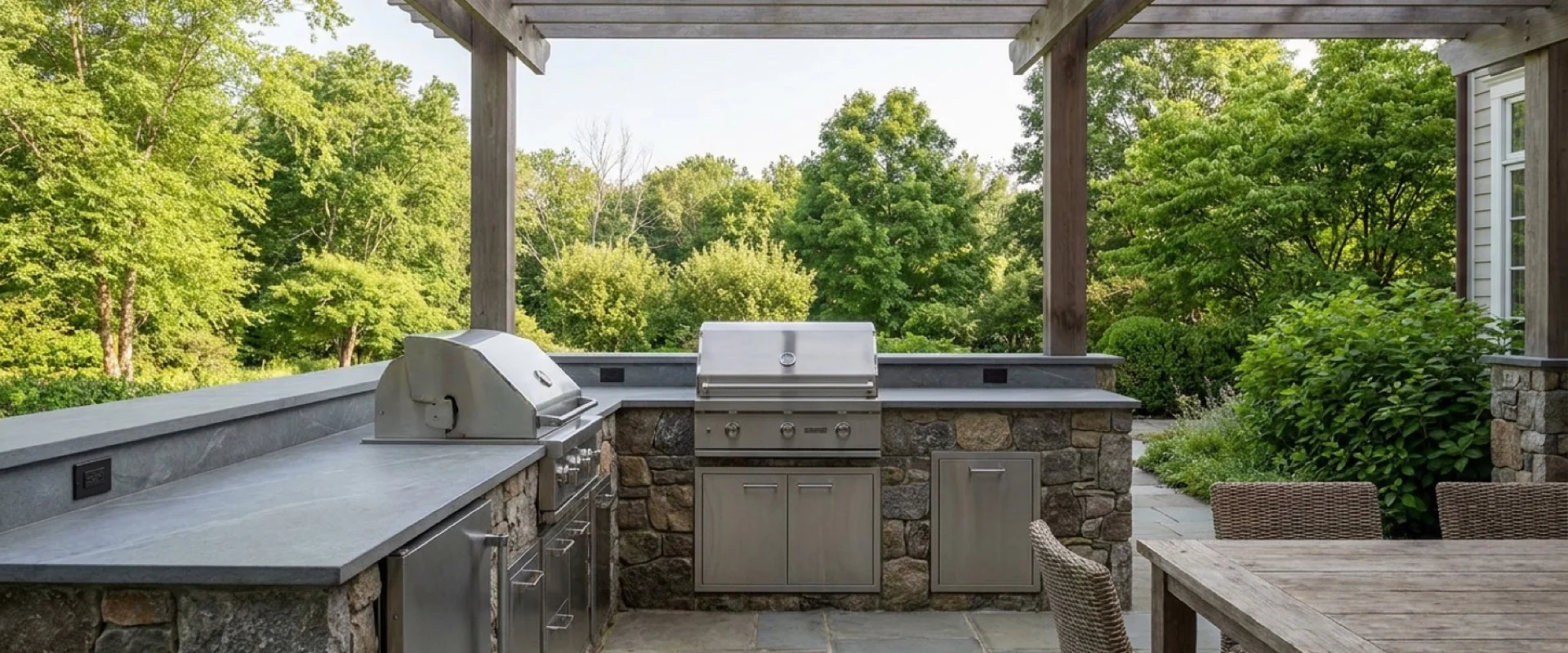 Outdoor kitchen with gray large-format porcelain counters beneath a timber pergola.