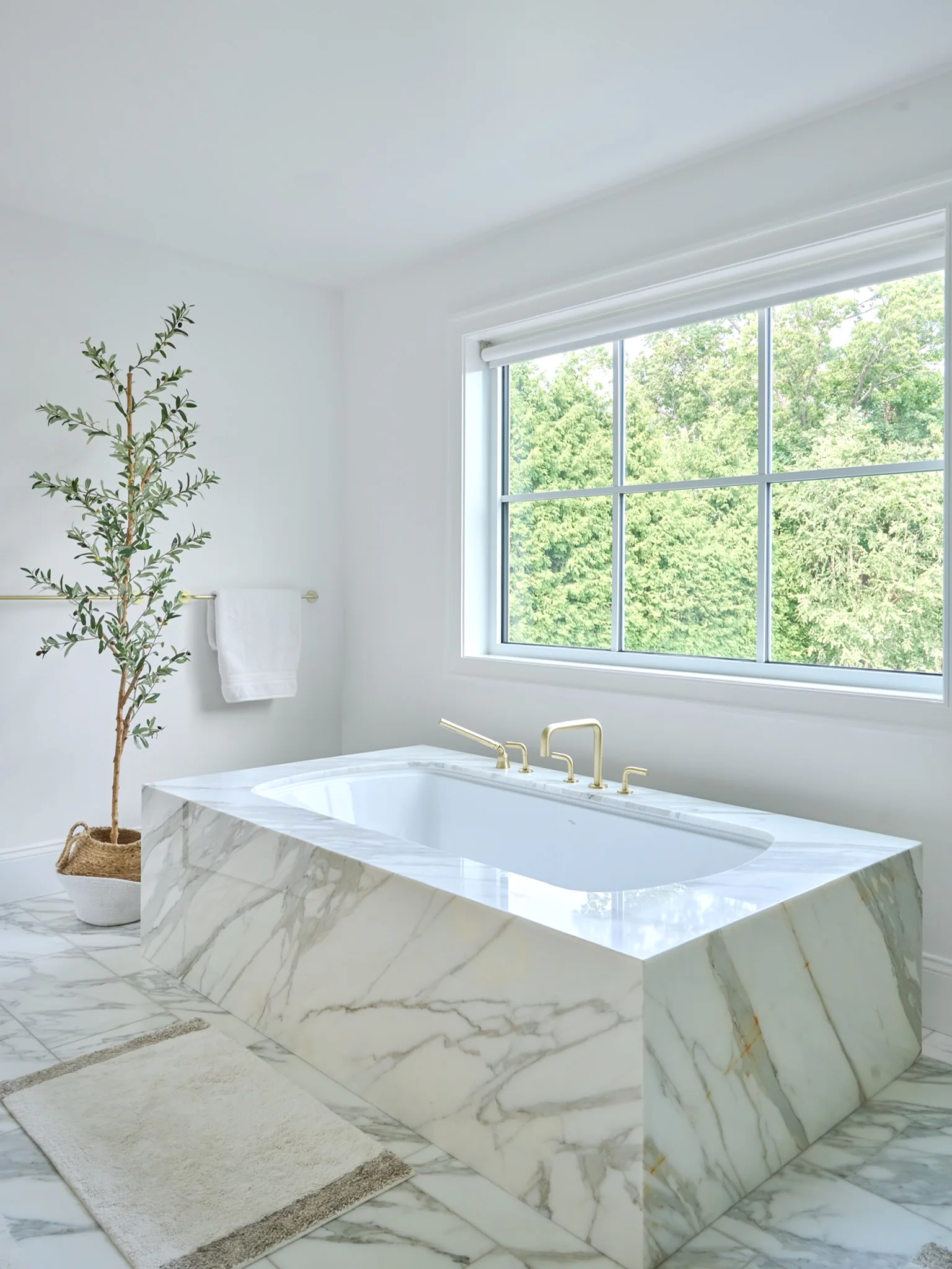 Calacatta Borghini marble tub surround with a mitred apron and brass deck-mounted fixtures.