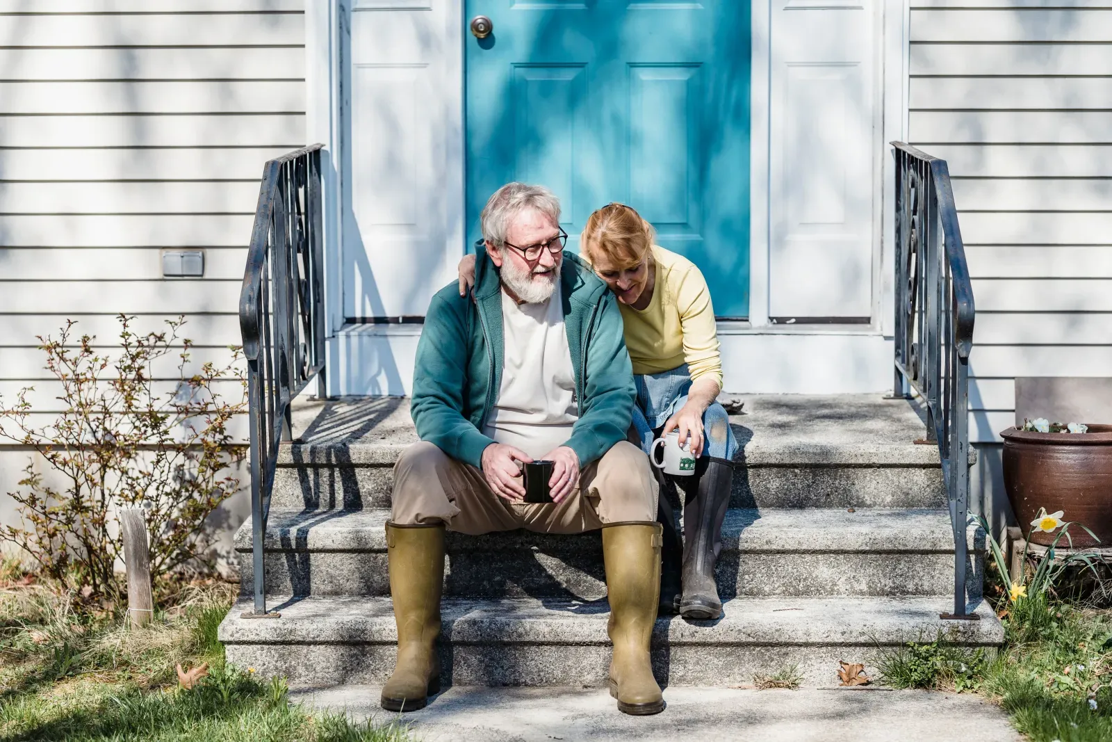 A mature couple sitting together on the front steps of their home.