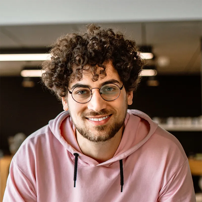 A man with curly hair wearing glasses and a pink hoodie.