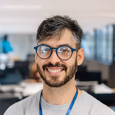 Smiling man with round glasses and a beard in an office setting.