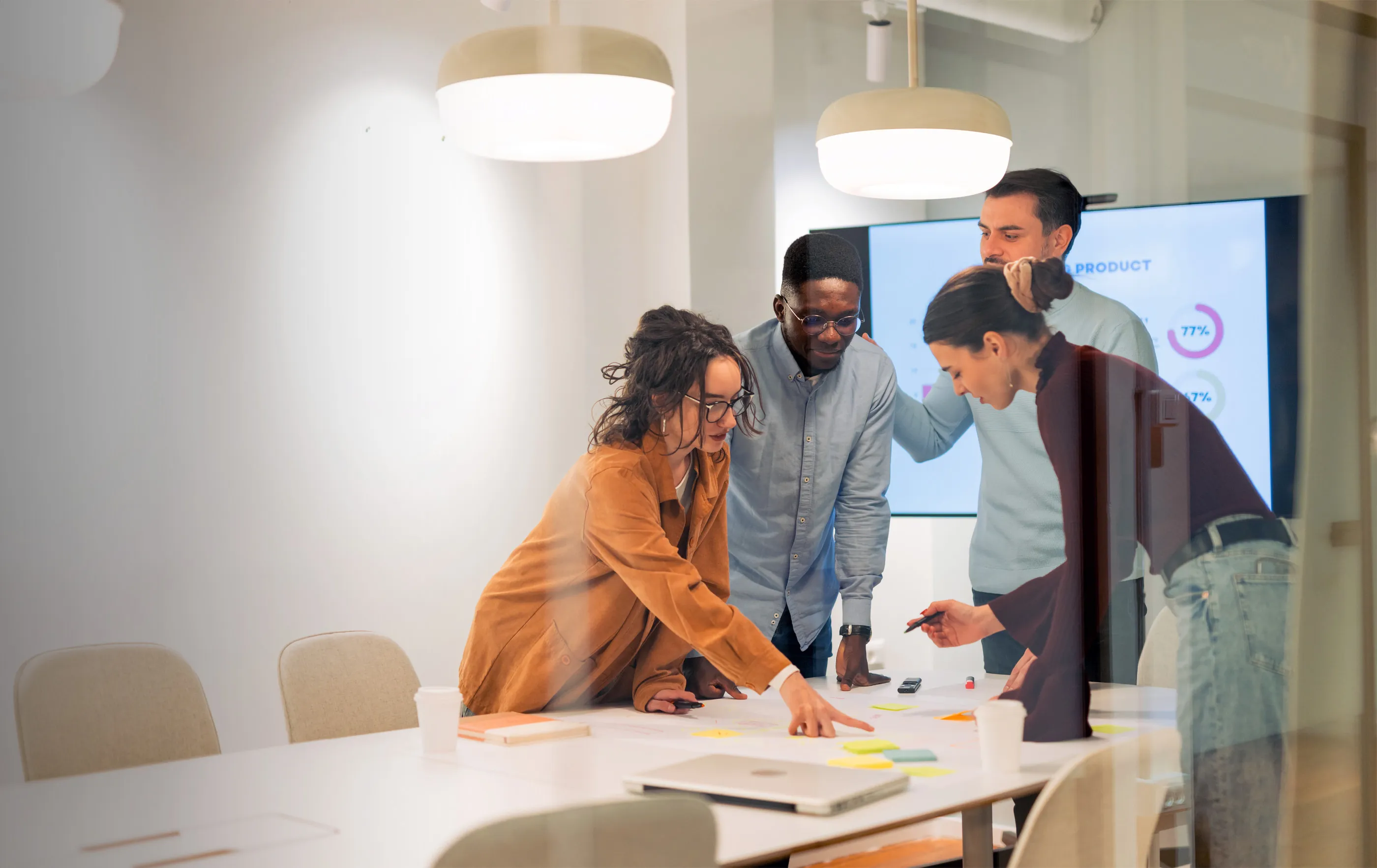 Four diverse colleagues collaborating and discussing notes on a table in a modern meeting room.
