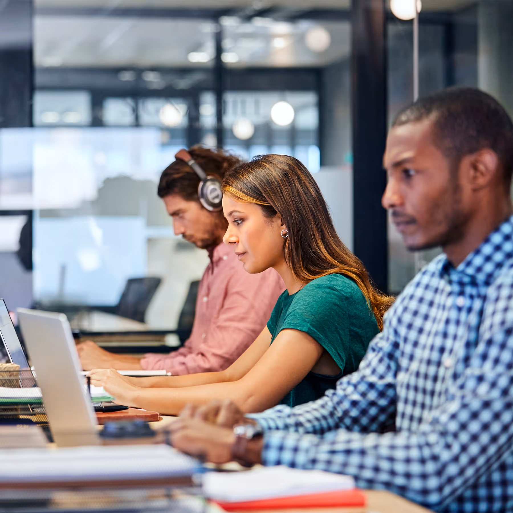 Three diverse young professionals working focused on laptops in a modern office.
