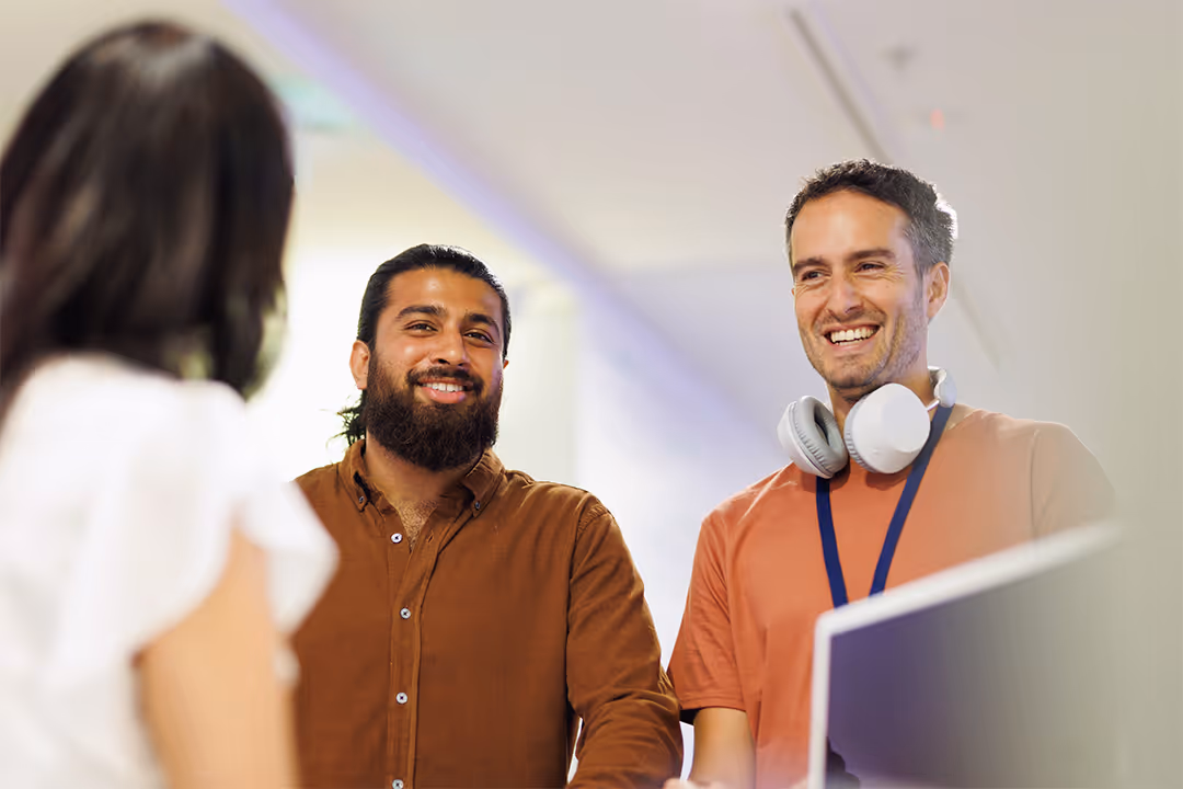 Two men smiling and talking to a woman in an office setting.