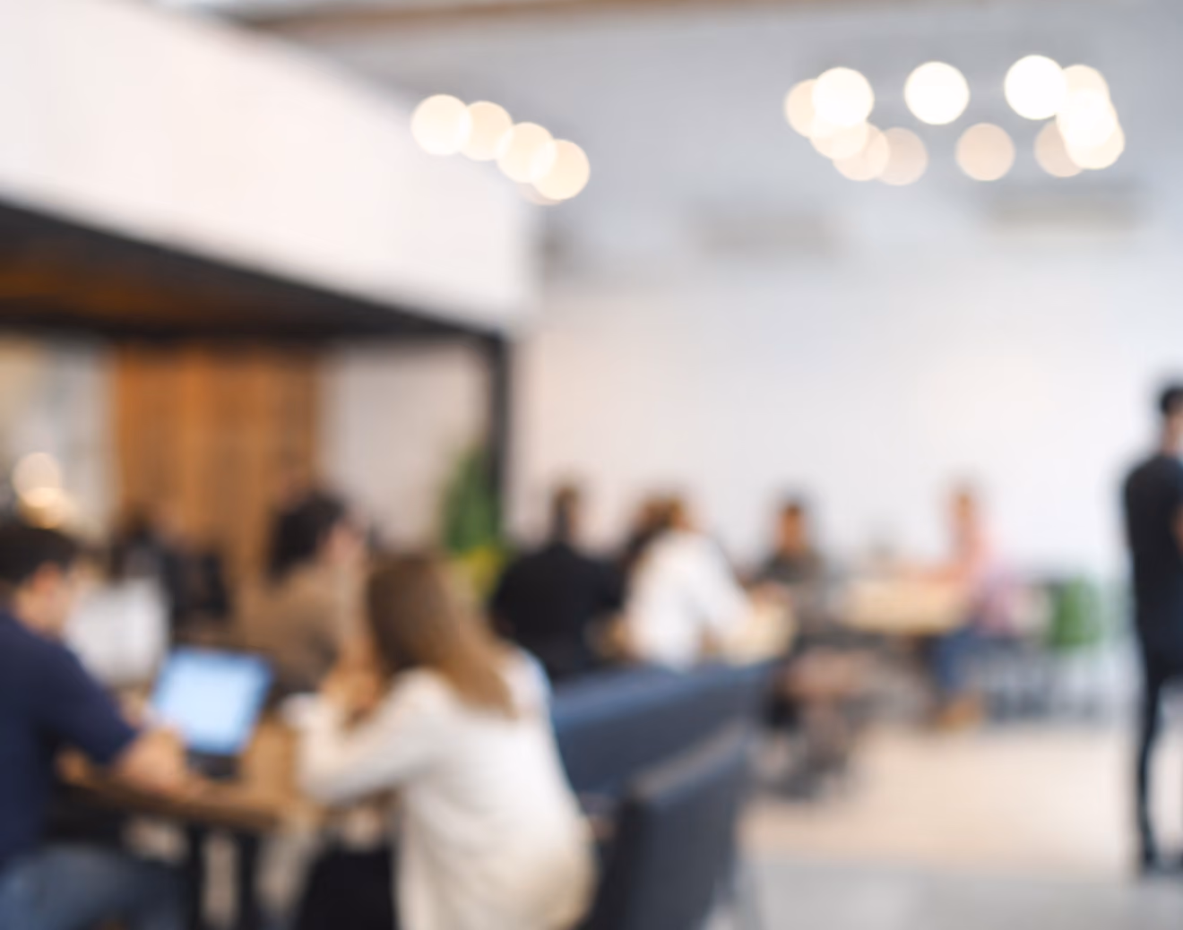 Blurred image of people sitting and working in a bright, modern indoor workspace.