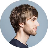 Profile of a young man with light brown hair and a short beard against a gray background.