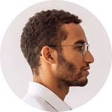 Profile of a man with short curly hair, beard, glasses, and a white collared shirt against white background.