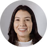 Smiling woman with dark hair wearing a white top against a light background.