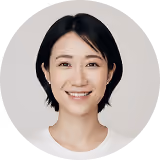 Smiling woman with short black hair wearing a white top on a white background.