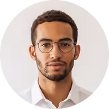 Young man with short curly hair and glasses wearing a white shirt looking straight ahead.