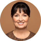 Smiling woman with dark hair wearing a leopard print top against a brown background.