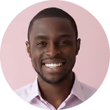 Smiling man with short hair wearing a light pink shirt against a pale pink background.