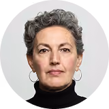 Portrait of a mature woman with short curly gray hair wearing hoop earrings and a black turtleneck.