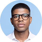 Close-up of a young man wearing round glasses and a white shirt, with a light blue background.