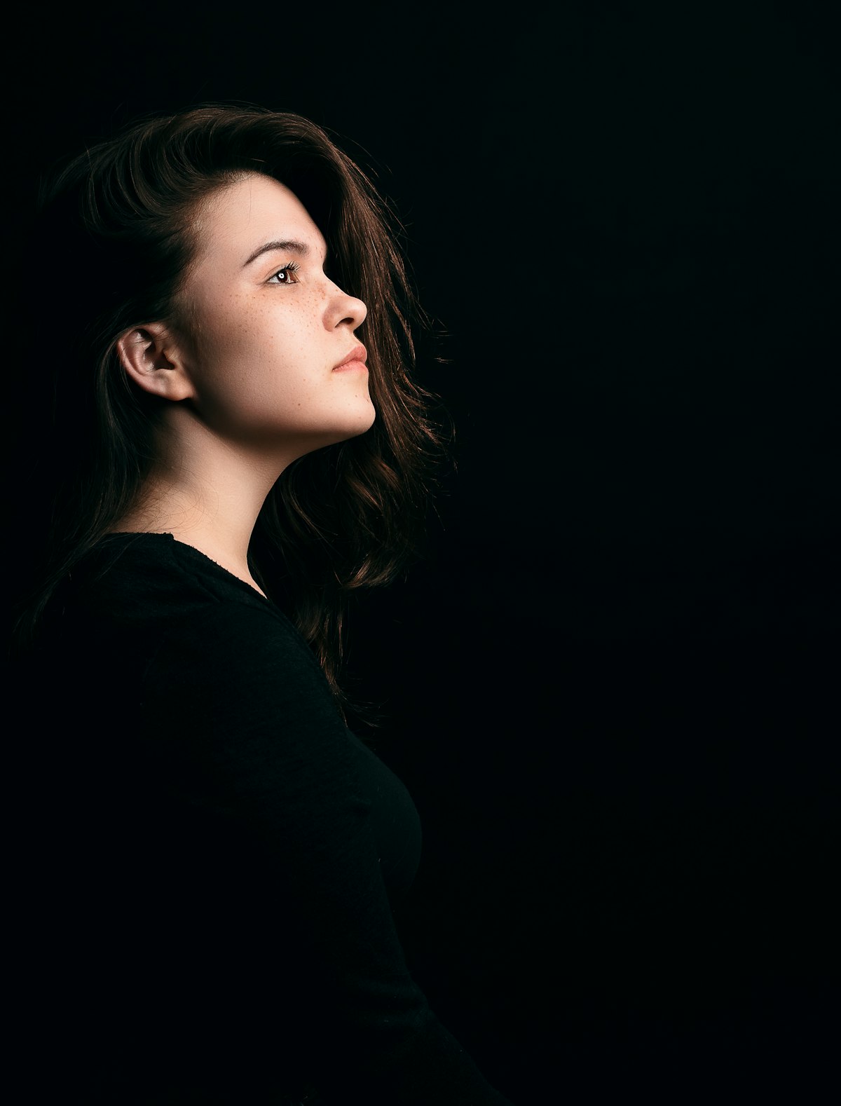 Profile portrait of a woman with dark hair against a black background, softly lit from the front