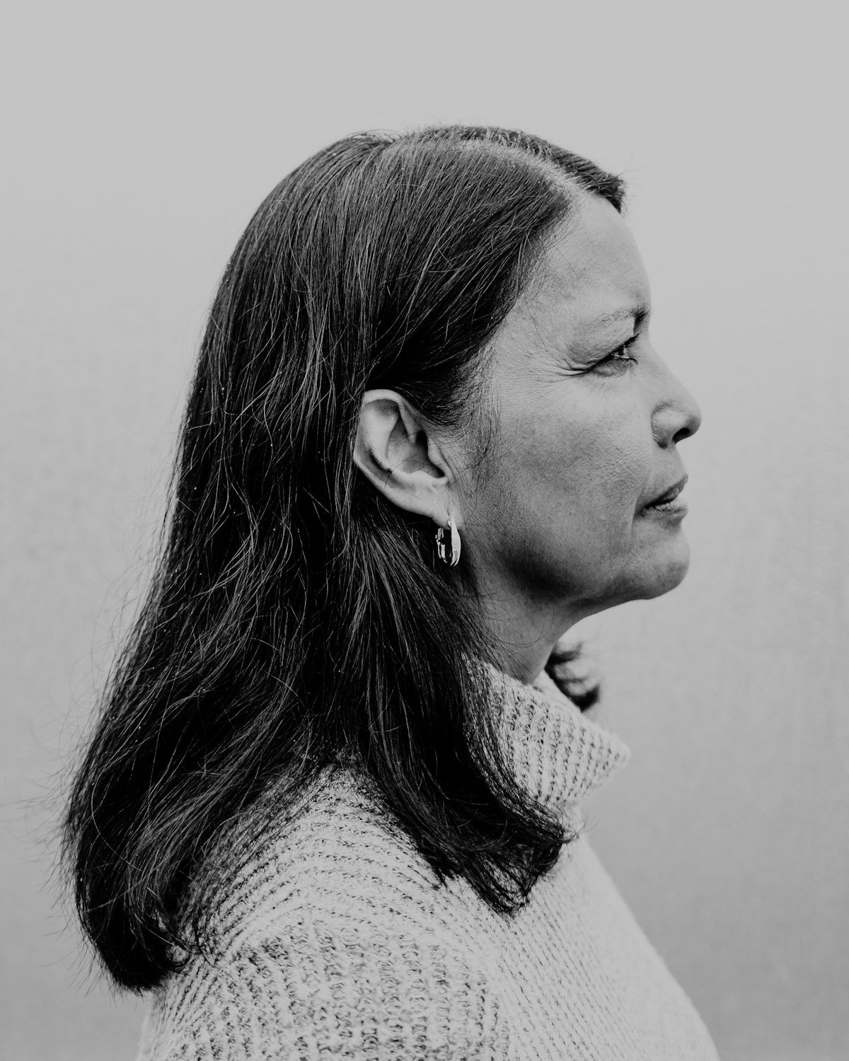 and white profile portrait of a woman in a knitted turtleneck against a plain background