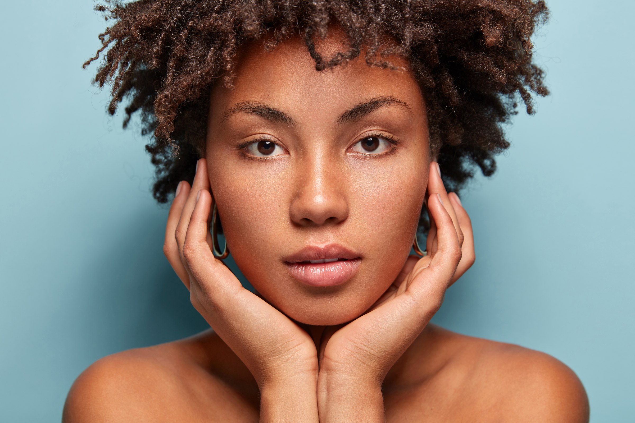 Portrait of a woman resting both hands against her cheeks, muted teal background