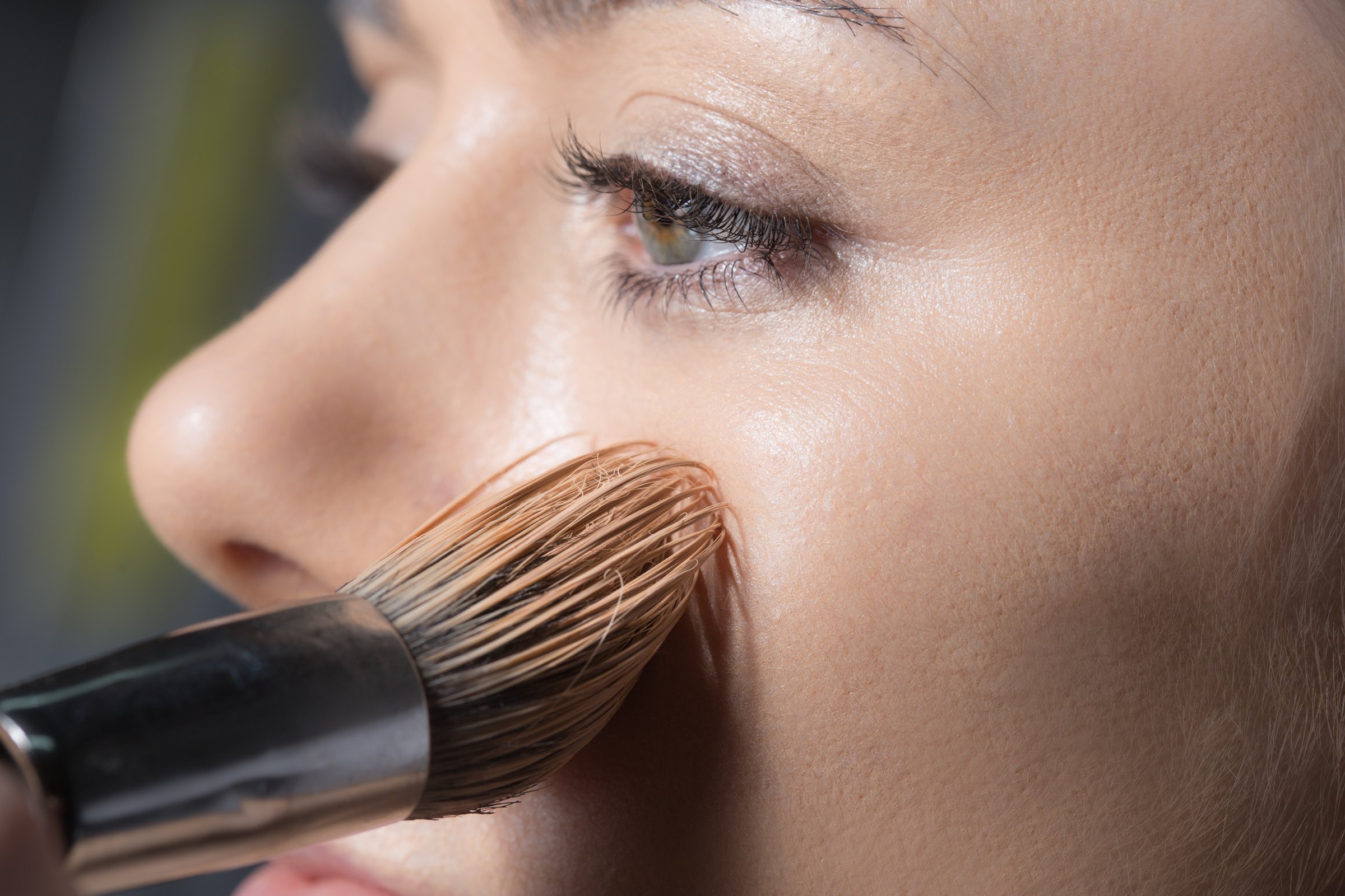 Profile close-up of a cheekbone catching soft light, a make-up brush at the edge of frame