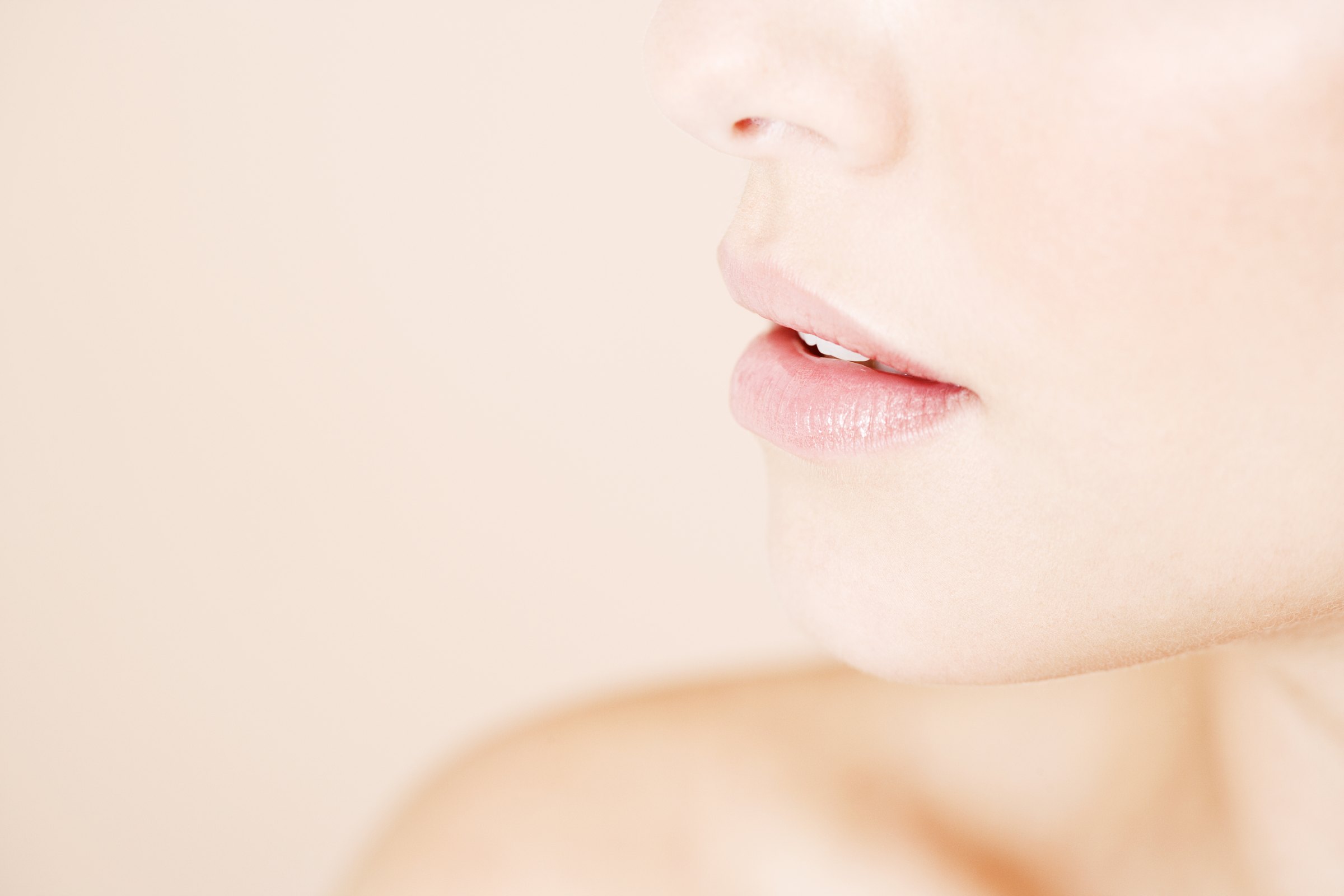 Soft profile close-up of a mouth and chin on a cream background