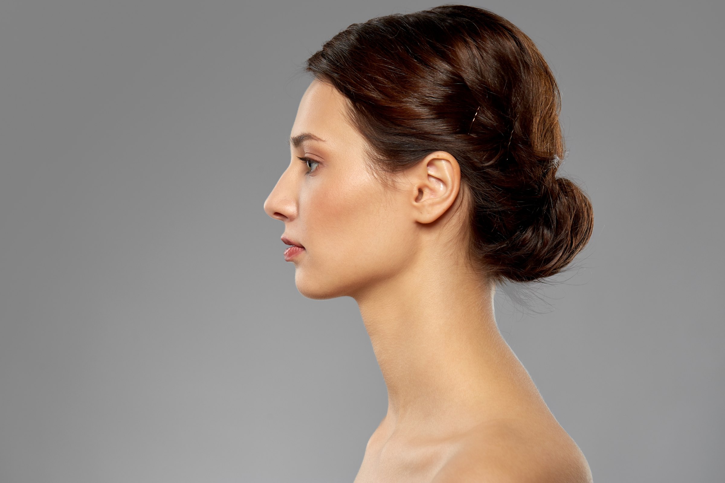 Profile portrait of a woman with her hair in a low bun against a grey background