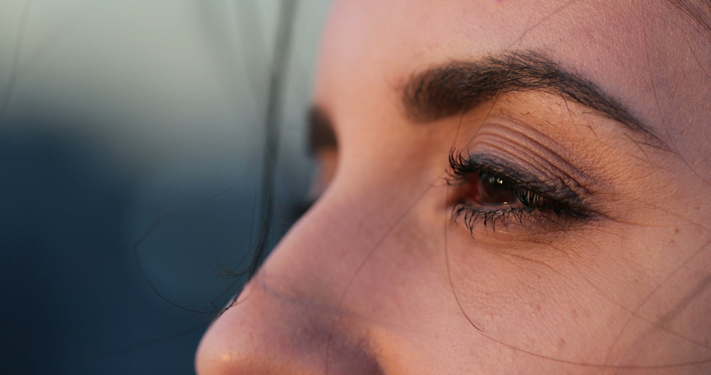 Three-quarter close-up of a brow and eye in warm, low light