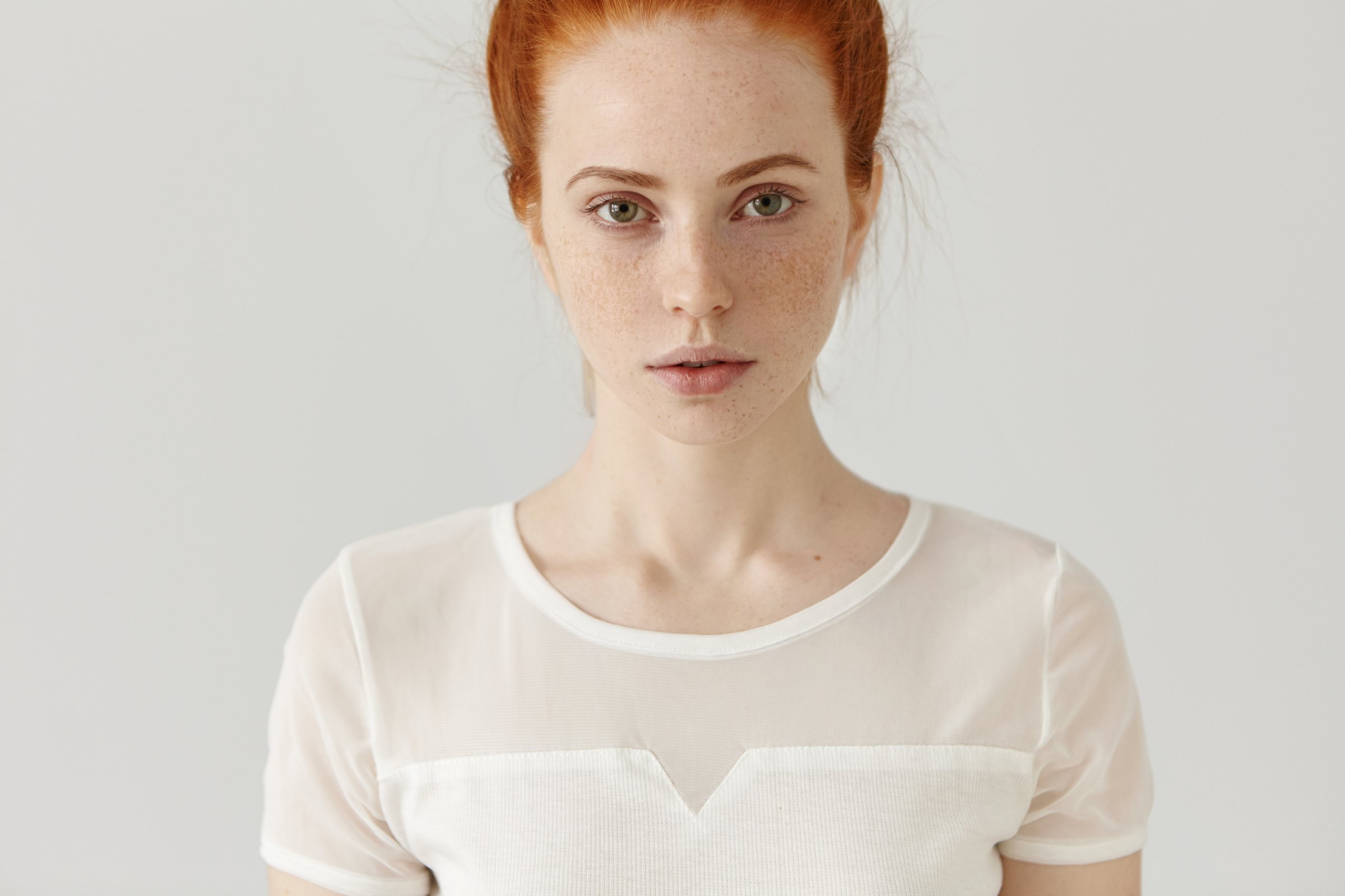 Portrait of a woman with red hair and freckled skin against a pale background
