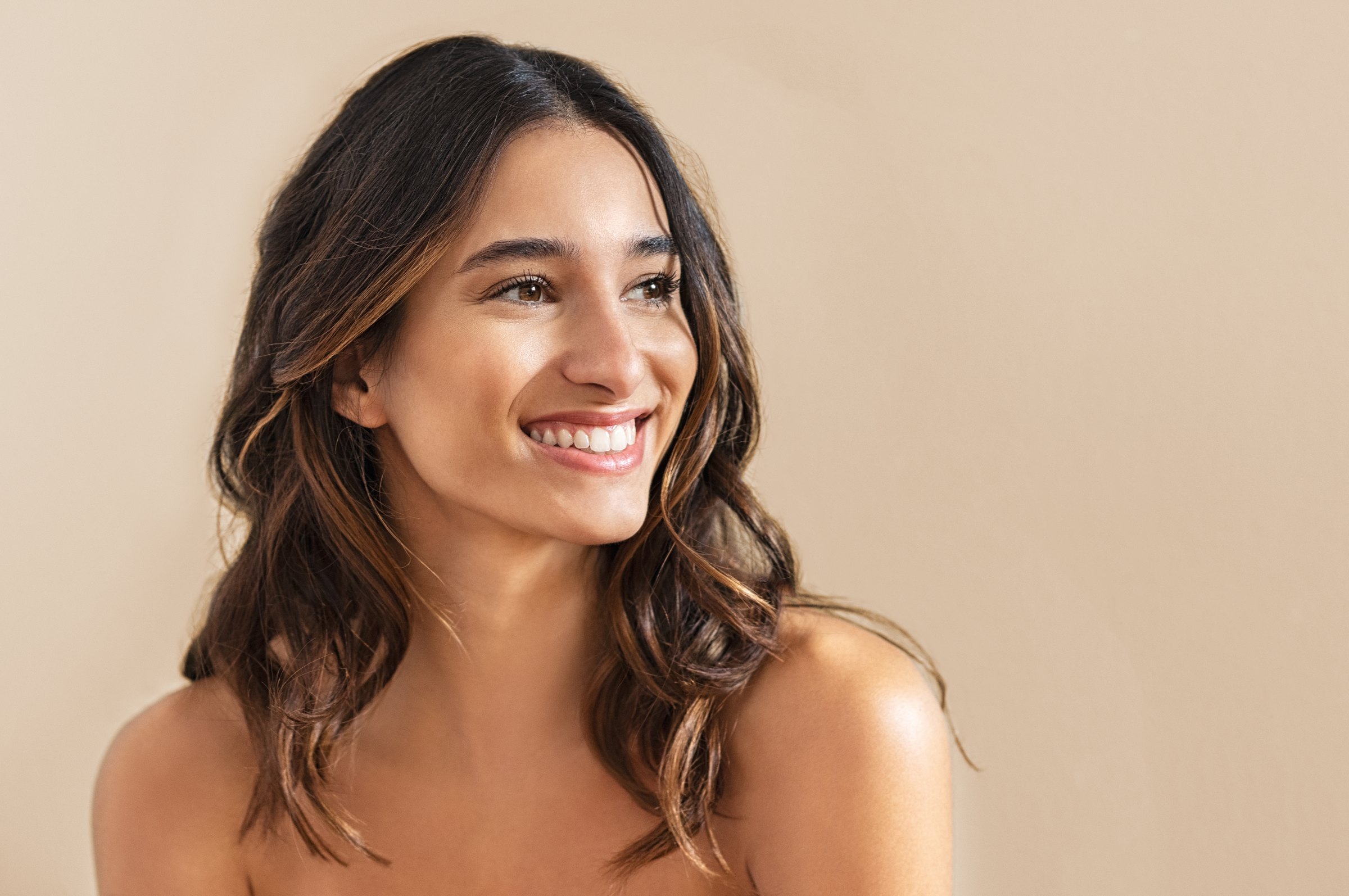 Smiling young adult woman with wavy brunette hair against a warm beige background